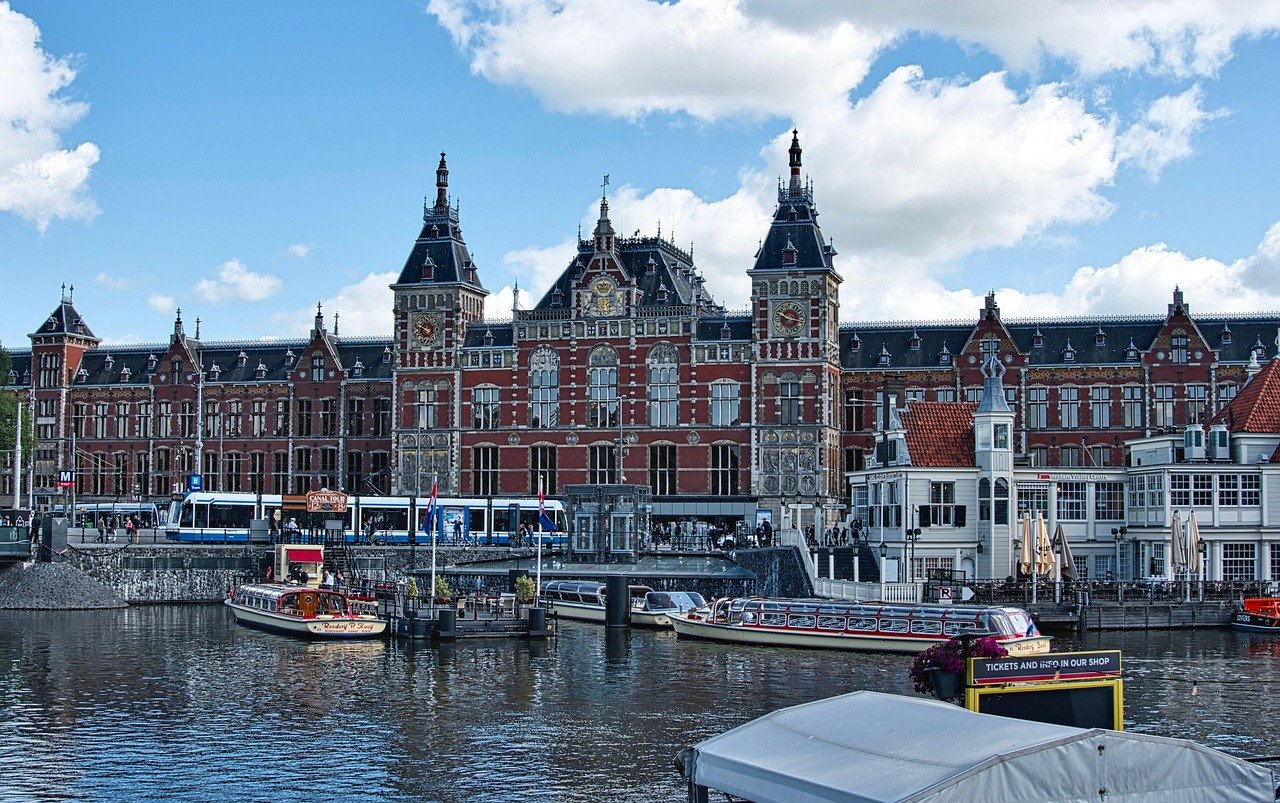 Historisch Amsterdam Centraal Station met grachtenboten en tram onder een heldere blauwe lucht in Nederland