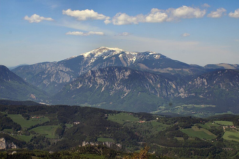Met sneeuw bedekte berg en groen valleilandschap Schilderachtig berglandschap met met sneeuw bedekte toppen, groene valleien en verspreide wolken onder een blauwe hemel