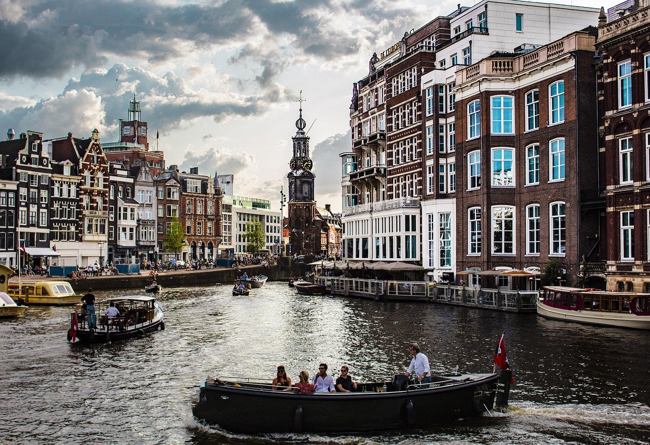Toeristen genieten van boottochten op een gracht omringd door historische gebouwen in Amsterdam onder een bewolkte hemel