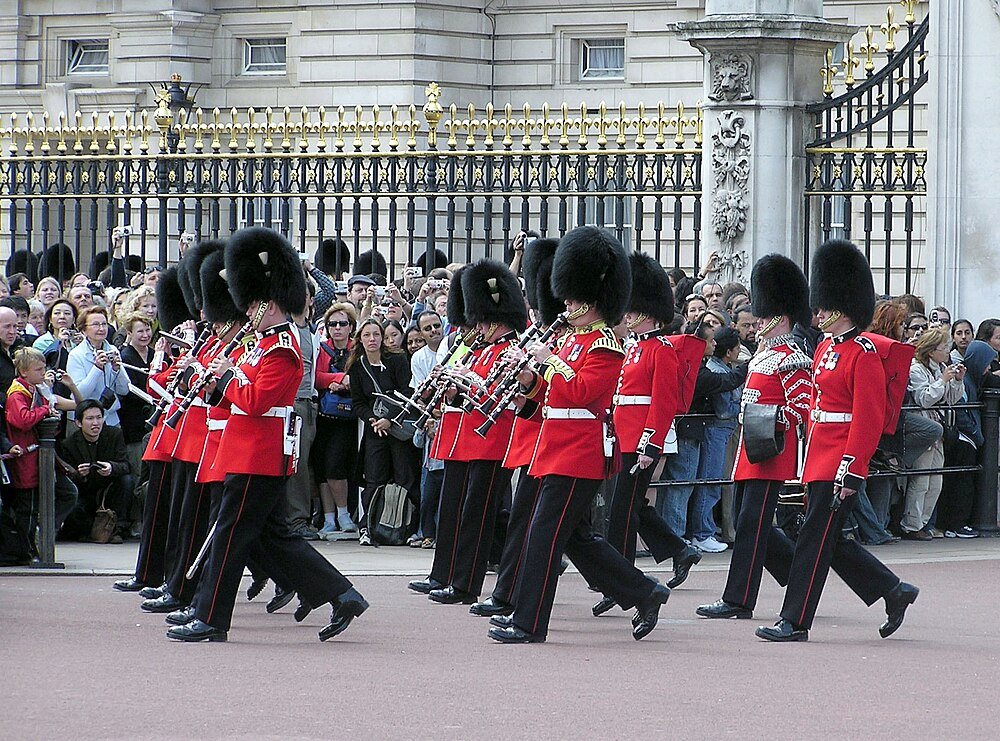 Britse wachters in rode uniformen en berenmutsen marcheren en spelen instrumenten bij ceremonie Buckingham Palace