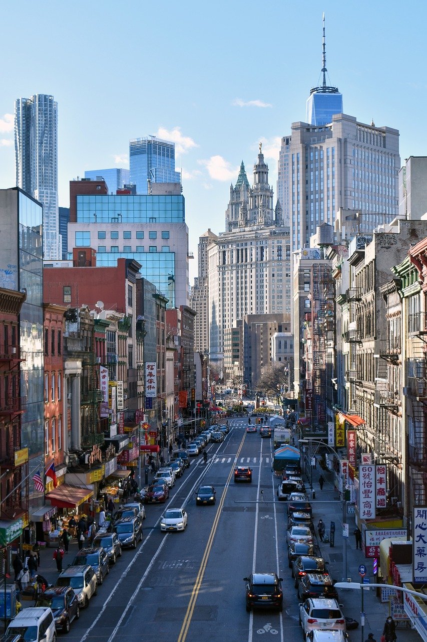 Drukke stedelijke straat in Chinatown met geparkeerde auto's, voetgangers en hoge wolkenkrabbers op de achtergrond onder een heldere hemel