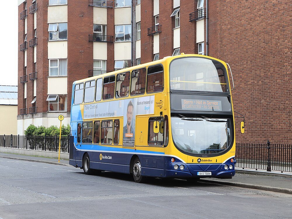 Dubbeldekker Dublin bus geparkeerd op stadsstraat met bakstenen gebouwen en advertentie op zijpaneel