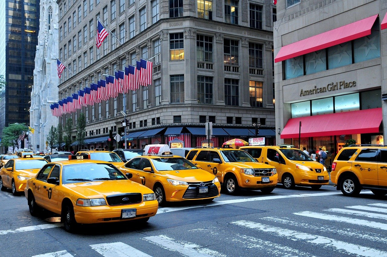 Gele New York City taxi's opgesteld in een drukke straat met Amerikaanse vlaggen en hoge gebouwen op de achtergrond