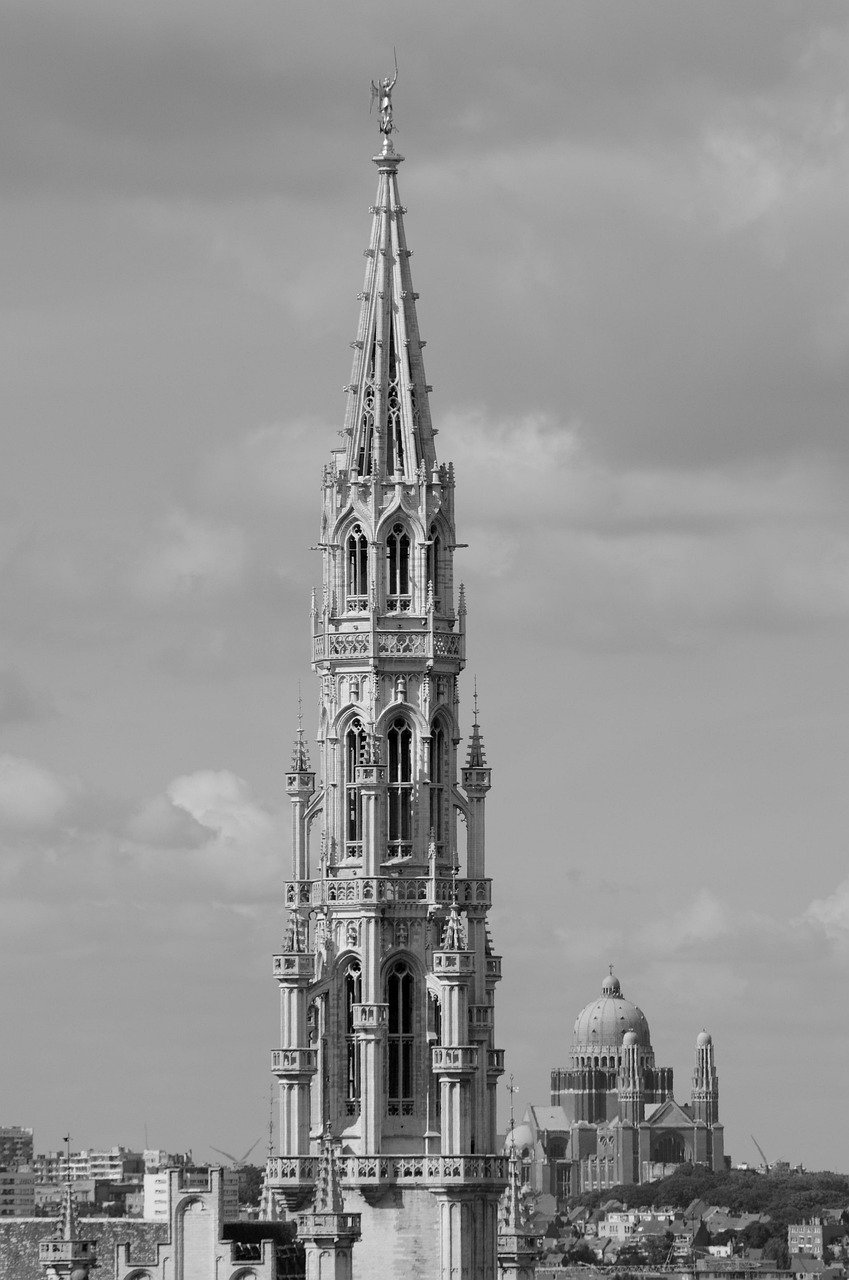 Gotische hoge kerktoren met ingewikkelde details en een standbeeld bovenop onder een bewolkte hemel in een stedelijke omgeving