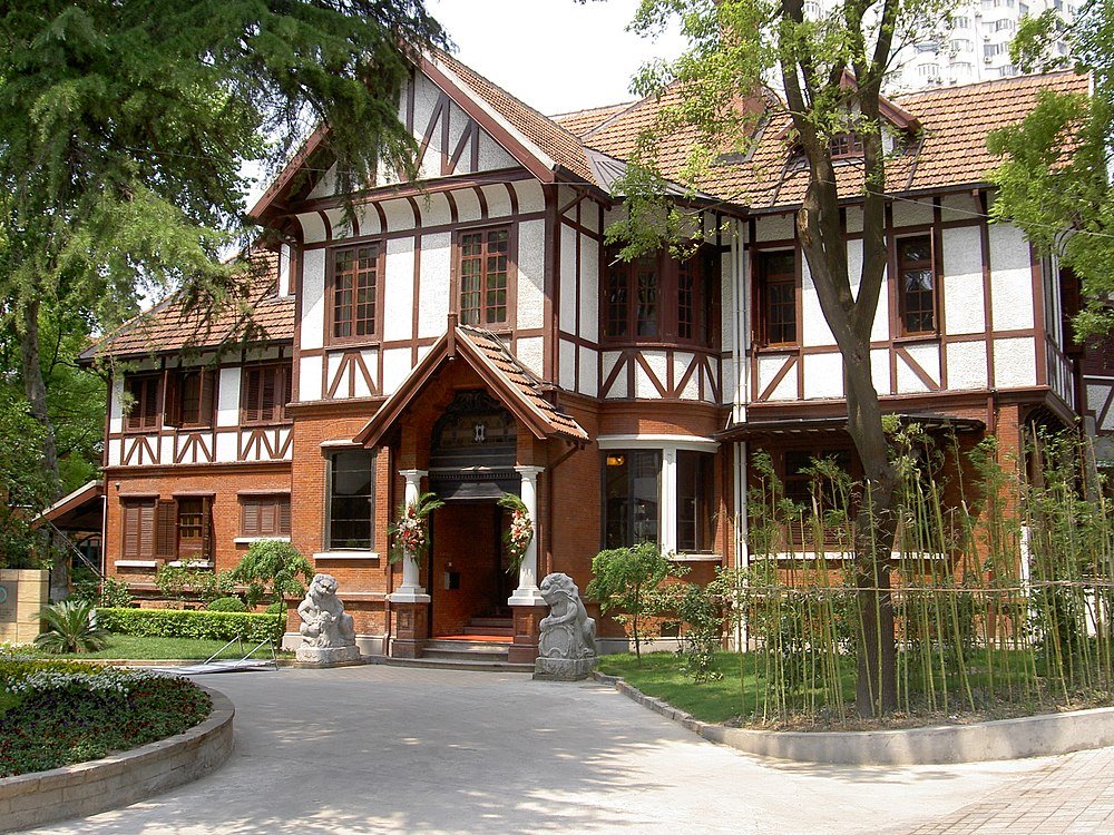 Huis in Tudor-stijl met bakstenen en houten gevel Groot huis in Tudor-stijl met bakstenen en houten gevel omgeven door bomen en tuin in zonnig weer