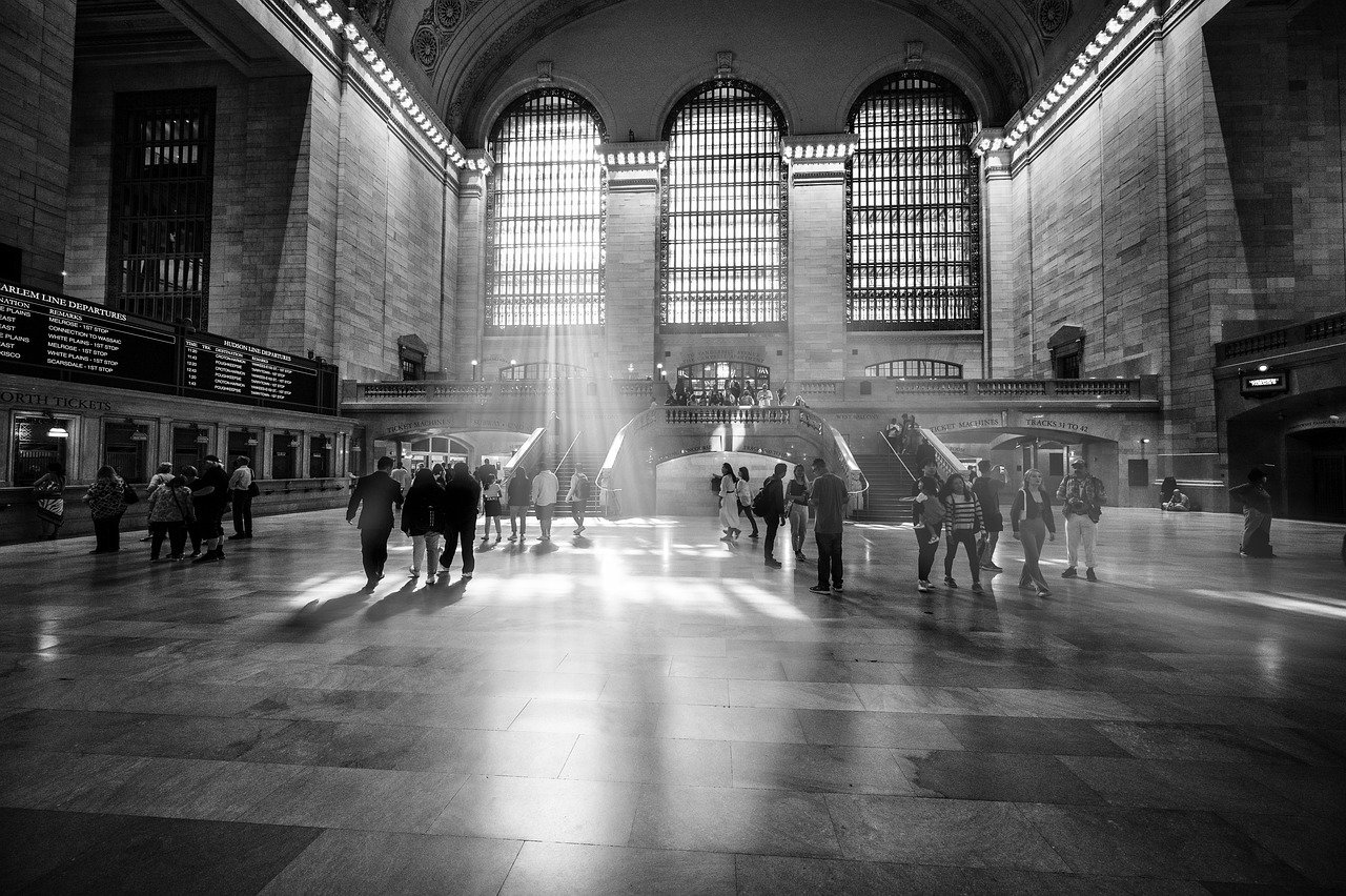 Zwart-wit afbeelding van Grand Central Terminal met zonlicht dat door grote ramen stroomt en mensen die binnen lopen
