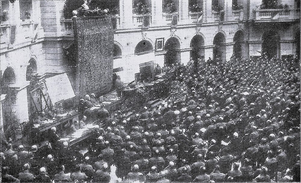 Historische menigte bij formeel buitenevenement in binnenplaats Historische zwart-wit foto van een grote menigte die een formeel buitenevenement bijwoont in een binnenplaats met bogen