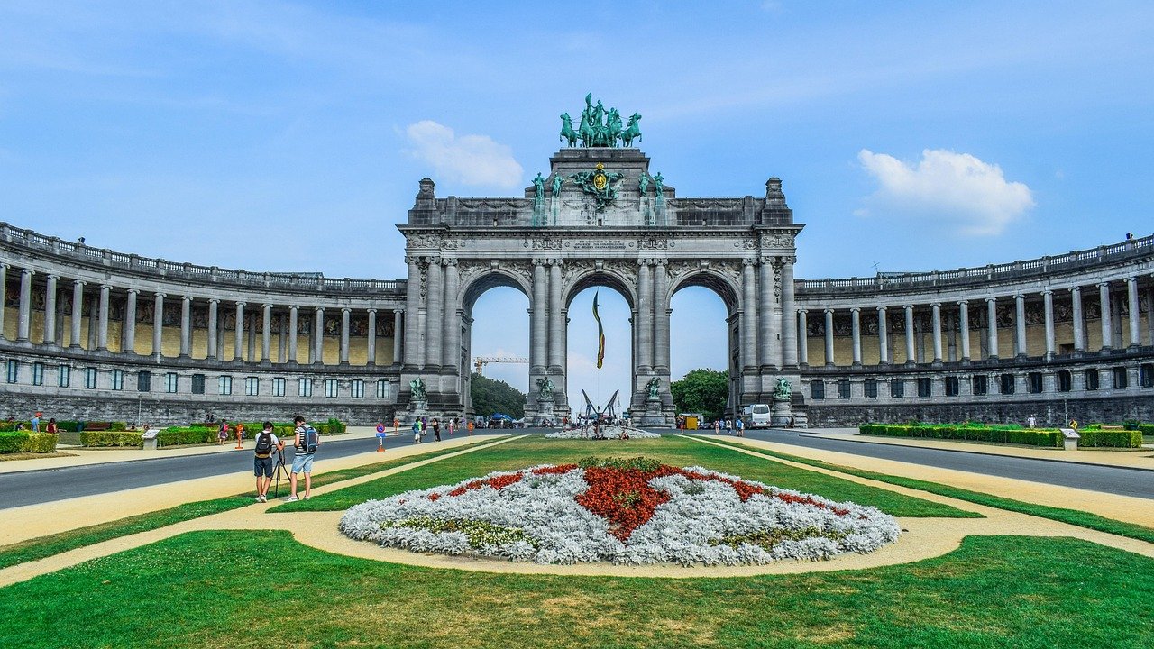 Triomfboogmonument met standbeelden en bloementuin in Brussels park onder blauwe lucht