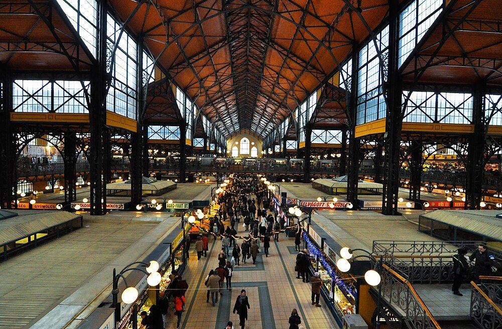 Historische Markthal Interieur met Shoppers Interieur van een grote historische markthal met hoge plafonds, ijzeren balken en talrijke shoppers die door kraampjes lopen