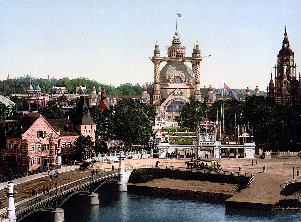 Historisch groot tentoonstellingsgebouw en brug in stadspark Historisch uitzicht op een groot tentoonstellingsgebouw met sierlijke architectuur, een brug over water en omliggende gebouwen in een stadspark.