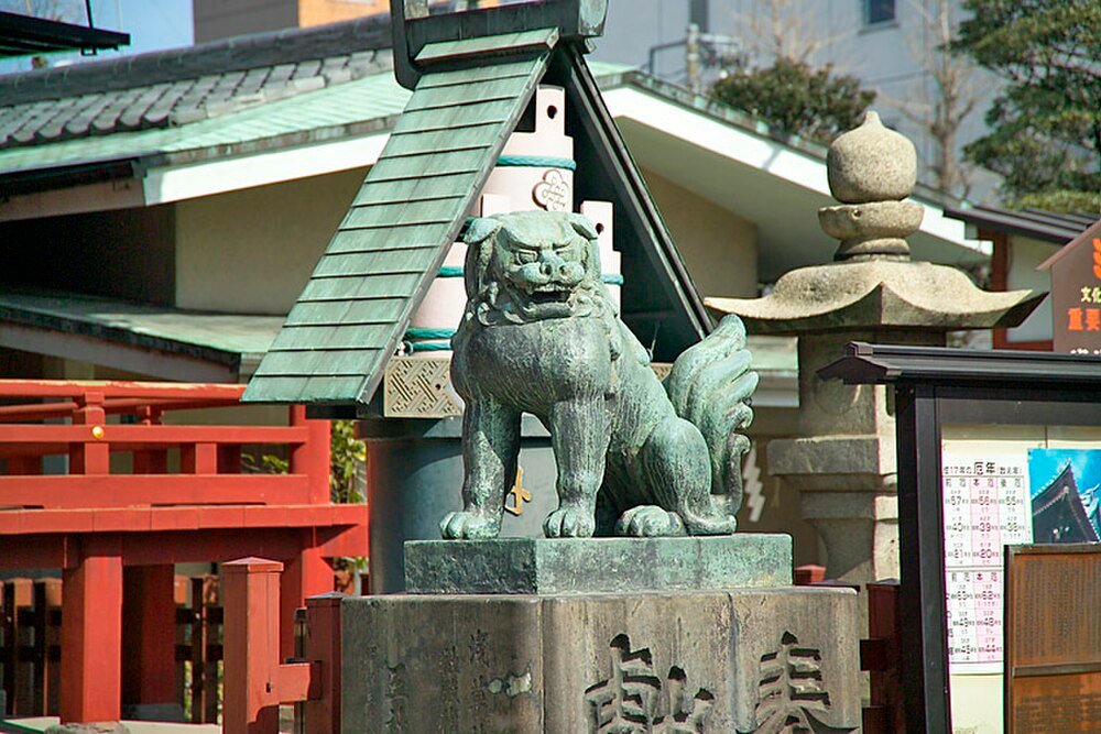 Bronzen Komainu Standbeeld bij Japans Heiligdom Bronzen komainu leeuw-hond standbeeld bij een traditioneel Japans heiligdom met rode houten relingen en stenen lantaarns