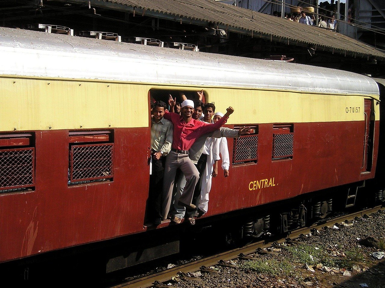 Groep jonge mannen die uit een rijdende trein in India hangen, vol opwinding en traditionele kleding nabij het Centraal station.