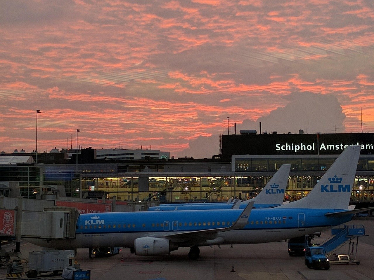 KLM-vliegtuigen geparkeerd op Schiphol tijdens een levendige zonsondergang met oranje en roze wolken in de lucht