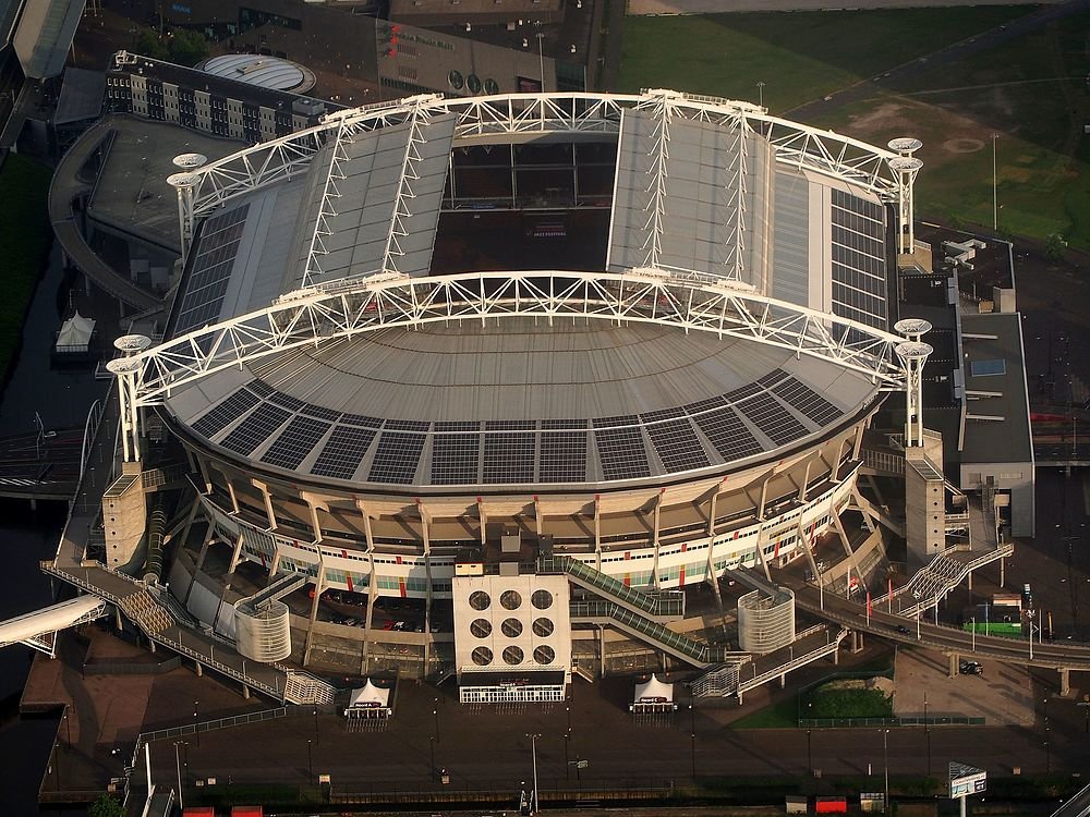 Luchtfoto van een groot modern stadion met een gedeeltelijk open dak en zonnepanelen op de dakconstructie