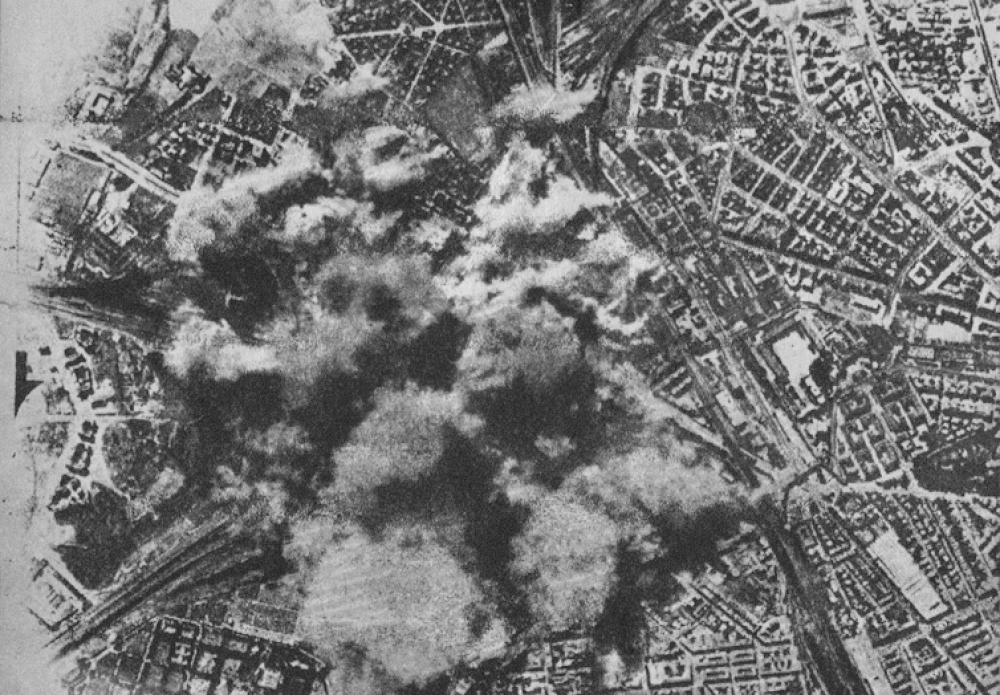 Luchtfoto van stedelijke explosie en rook in oorlogstijd Luchtfoto in zwart-wit die een grote explosie en rook boven een stedelijk gebied tijdens een bombardement in oorlogstijd toont.