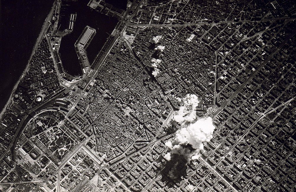 Luchtfoto van stad met explosie en rook Luchtfoto in zwart-wit van een stad met dichte bebouwing en rook die opstijgt van een explosieplaats