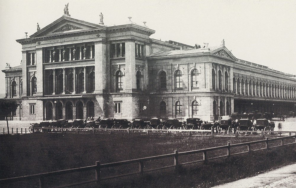 Historisch gebouw met paardenkoetsen Historische zwart-wit foto van een groot klassiek gebouw met paardenkoetsen geparkeerd buiten