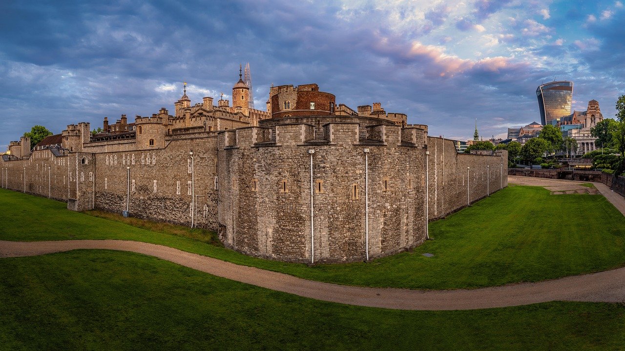 Historische Tower of London vesting met stenen muren en moderne stadsgezicht onder een bewolkte hemel bij zonsondergang