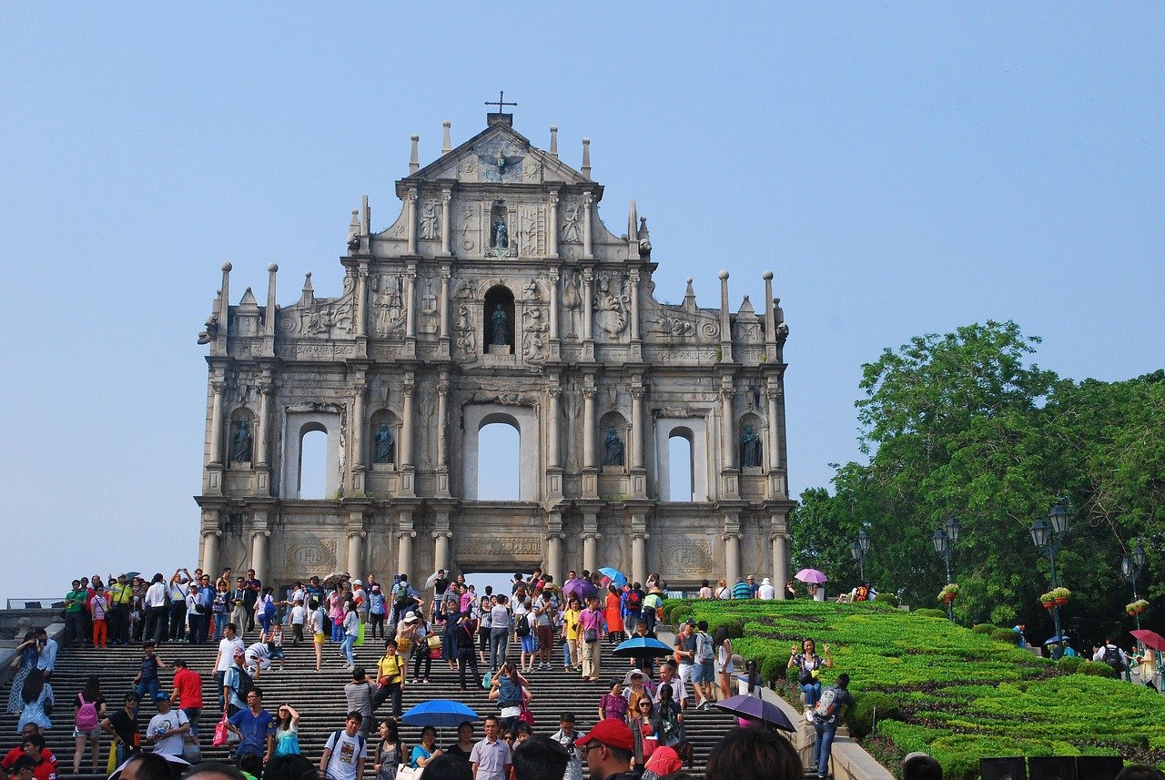 Ruïnes van de historische stenen gevel van St. Paul's met toeristen en groen onder een heldere blauwe lucht in Macau