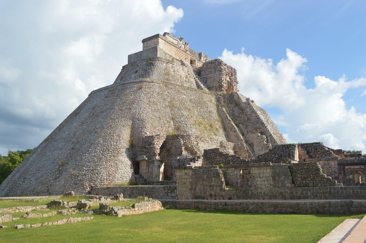 Oude Maya-piramide met stenen treden en ruïnes onder een blauwe hemel met wolken, die historische architectuur toont