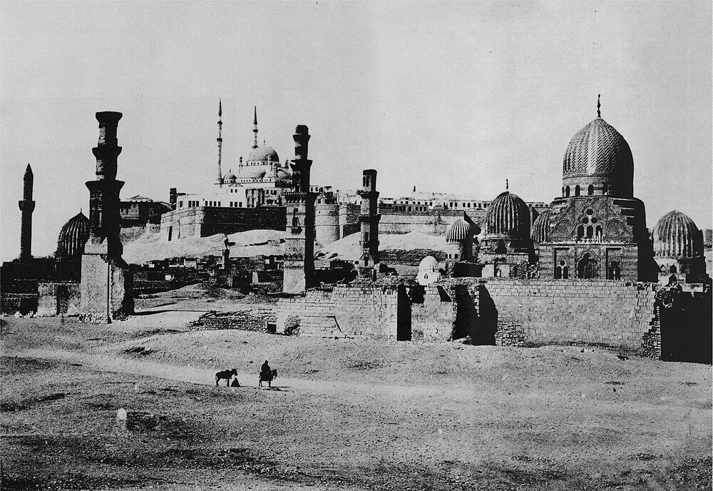 Historische zwart-witfoto van het oude islamitische Caïro met moskeeën, minaretten en koepels in woestijnlandschap
