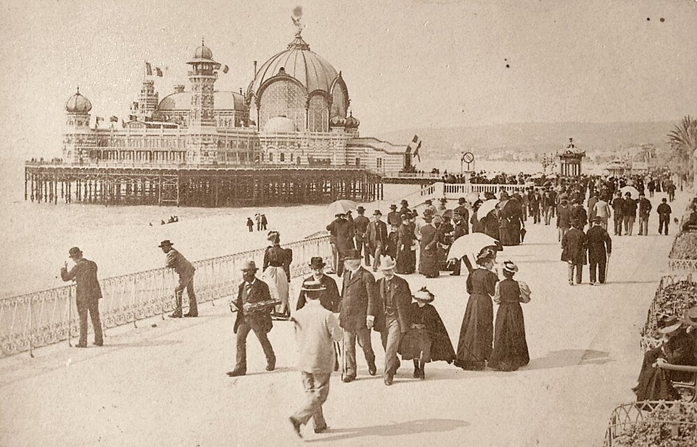 Vintage foto van Victoriaanse mensen die wandelen op een promenade aan zee nabij een grote sierlijke pierpaviljoen