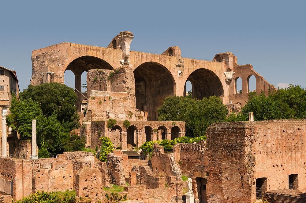 Oude Romeinse ruïnes met grote bogen en bakstenen structuren omgeven door groen onder een heldere blauwe hemel