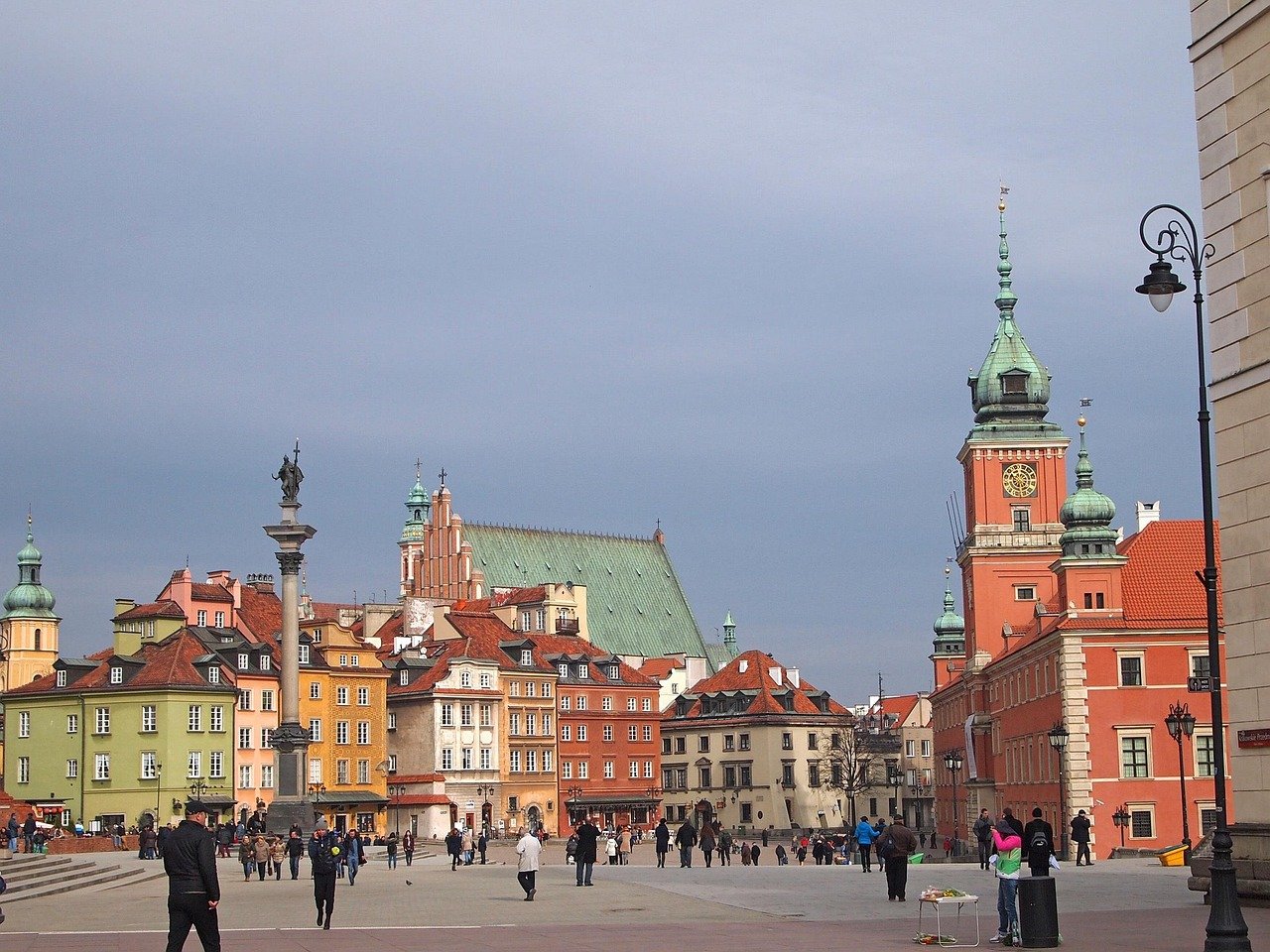 Kleurrijke historische gebouwen en een klokkentoren op het oude stadsplein van Warschau, Polen met mensen die rondlopen.