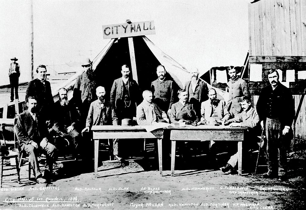 Eerste Raadsvergadering Stadhuis 1886 Historische zwart-wit foto van de eerste gemeenteraad van het stadhuis in 1886 met mannen in pakken en een tent met het opschrift City Hall