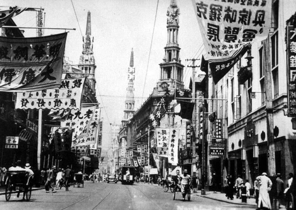 Historische zwart-wit straatbeeld in het vroege 20e-eeuwse Shanghai met traditionele Chinese banners en riksja's