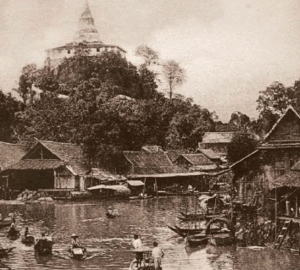 Historisch dorp aan de rivier met tempel op een heuveltop Historisch dorp aan de rivier met traditionele houten huizen en boten nabij een tempel op een heuveltop in Zuidoost-Azië