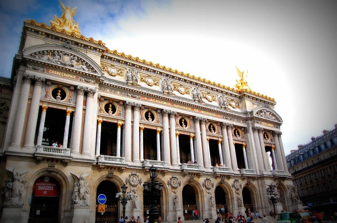 Voorgevel van het Palais Garnier operahuis in Parijs met sierlijke zuilen en gouden beelden onder een blauwe hemel