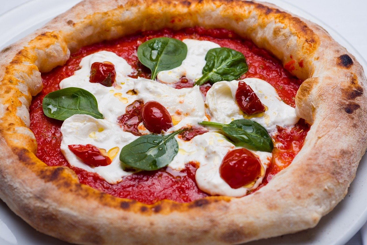 Close-up van een heerlijke Napolitaanse pizza met verse tomatensaus, mozzarella kaas, spinaziebladeren en cherrytomaten