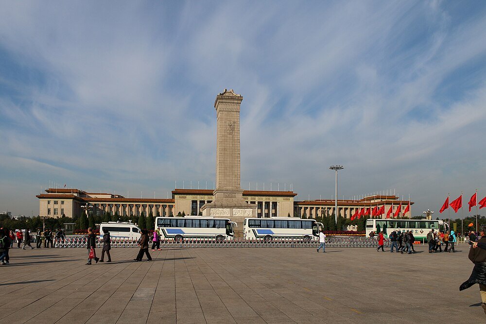 Tiananmenplein met Monument en Bezoekers Tiananmenplein in Beijing met Monument voor de Helden van het Volk, bussen, rode vlaggen en toeristen onder een blauwe lucht