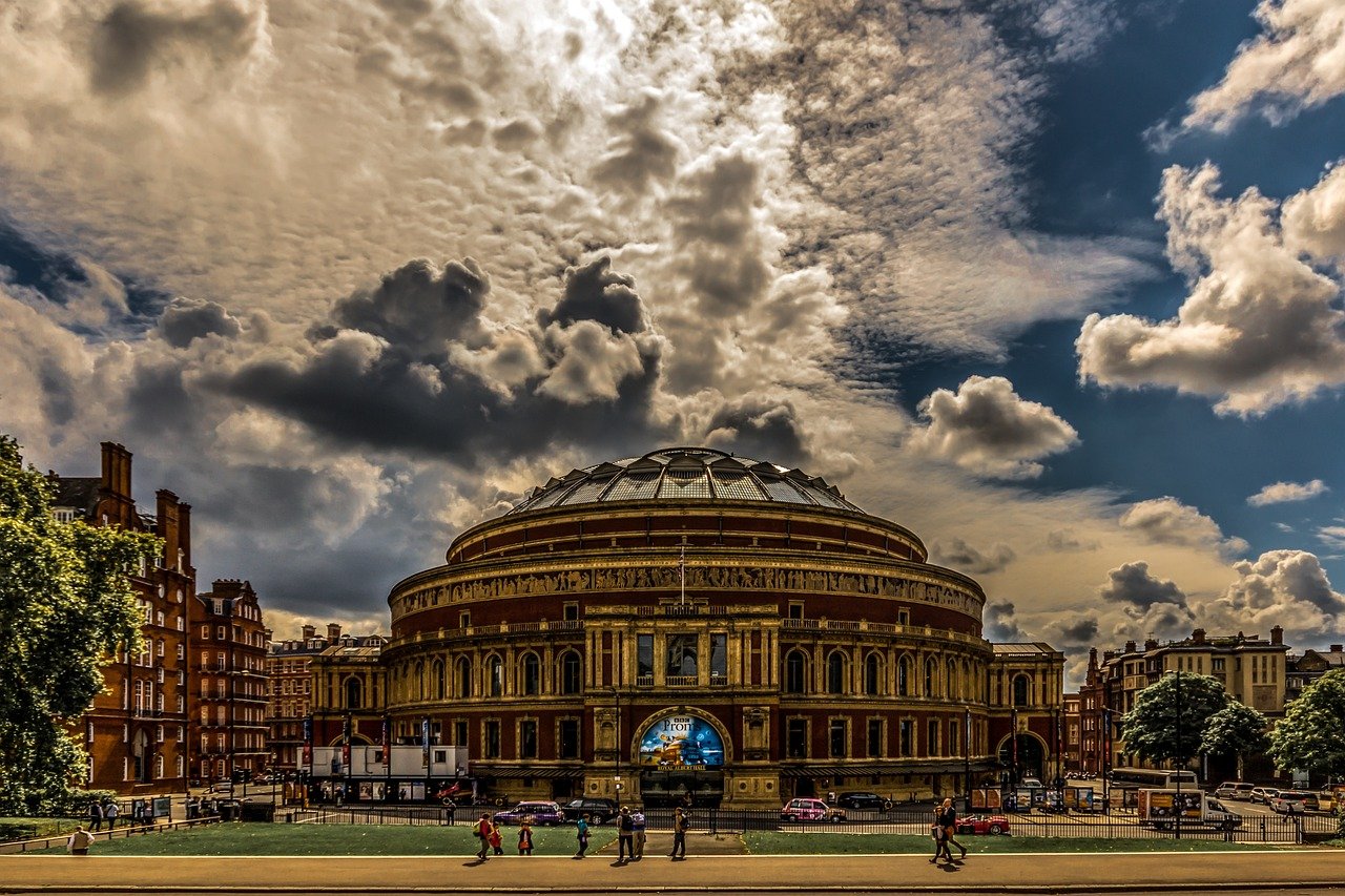 Royal Albert Hall in Londen met dramatische bewolkte lucht en mensen die ervoor lopen, historisch concertgebouw en herkenningspunt