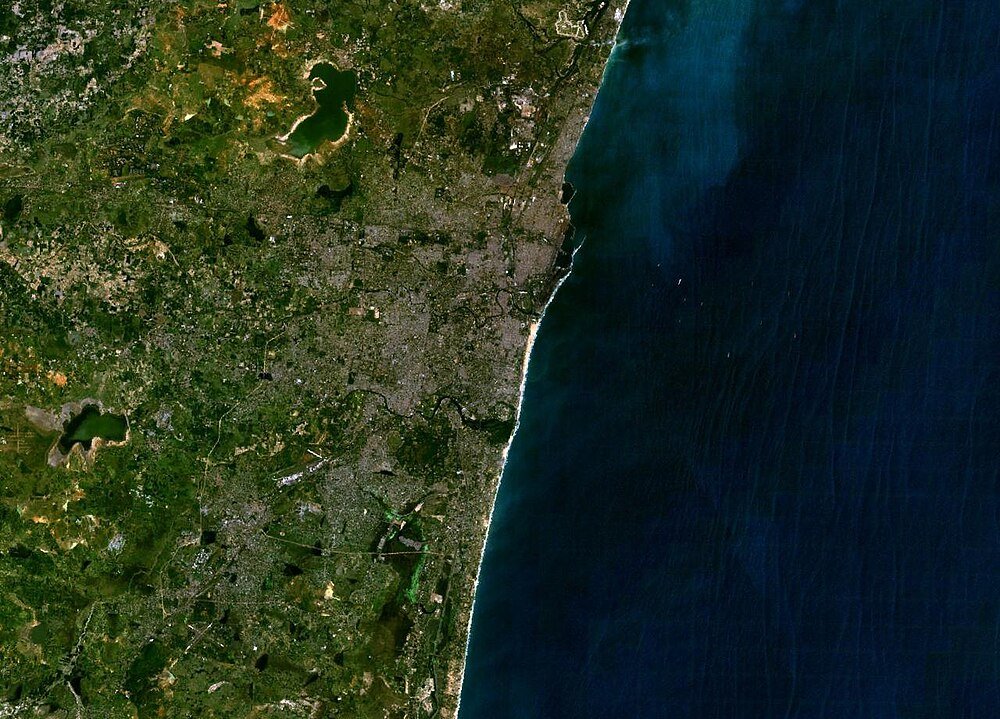 Satellietbeeld van kuststad en oceaan Satellietbeeld van een kuststad met stedelijke gebieden, groene landschappen en oceaankustlijn, met gedetailleerde land- en waterkenmerken.
