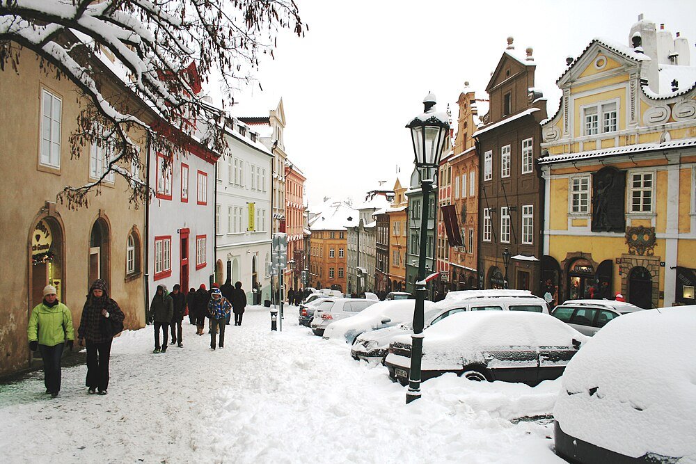 Met sneeuw bedekte straat met geparkeerde auto's en mensen die lopen in de buurt van kleurrijke historische gebouwen in een Europese stad tijdens de winter