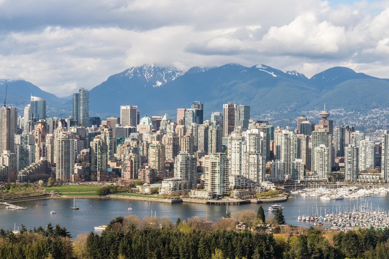Skyline van Vancouver met moderne hoogbouw, waterkant en bergen op de achtergrond onder bewolkte lucht