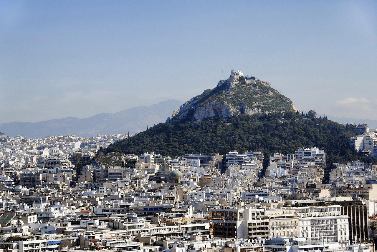 Panoramisch uitzicht op de stadsgezichten van Athene met de met groen bedekte berg Lycabettus en gebouwen onder een heldere blauwe hemel