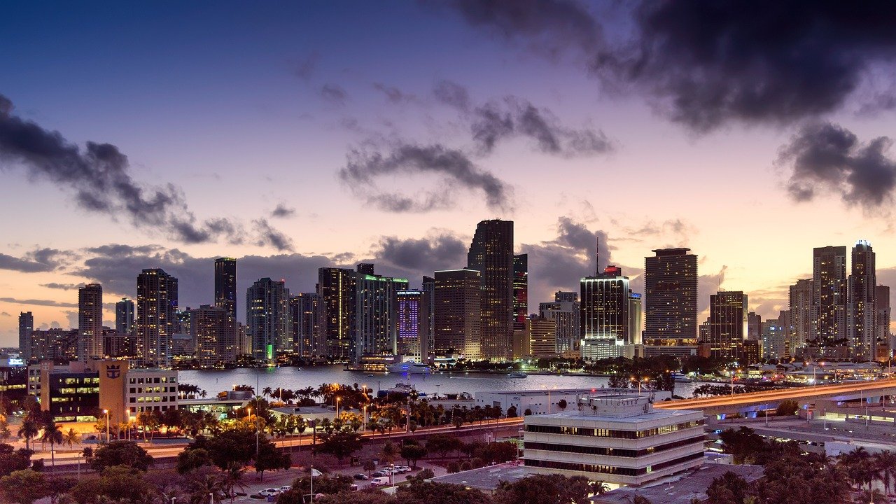 Miami stadsgezicht bij schemering met verlichte wolkenkrabbers en uitzicht op de waterkant onder een bewolkte paarse hemel