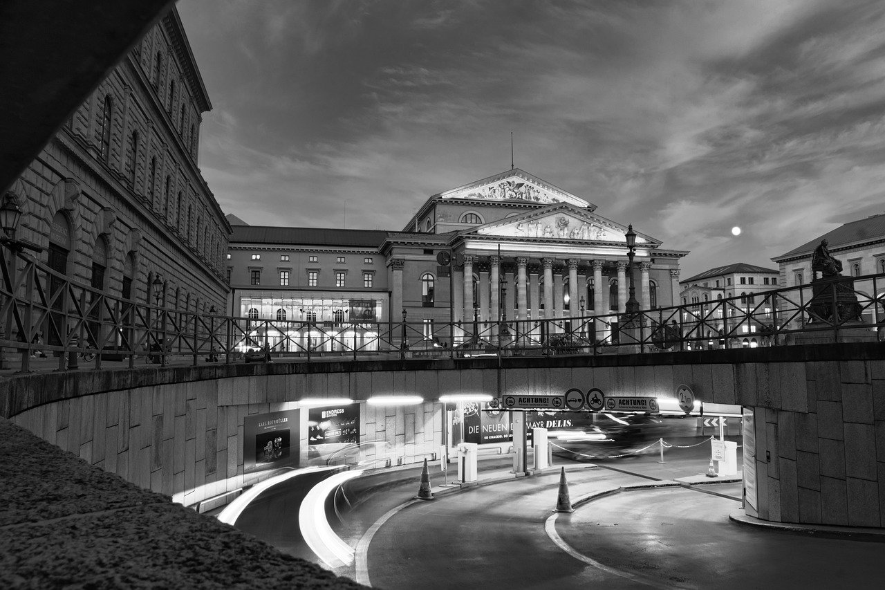 Zwart-wit foto van historisch Europees gebouw met zuilen en gebogen weg met lichtsporen in de schemering