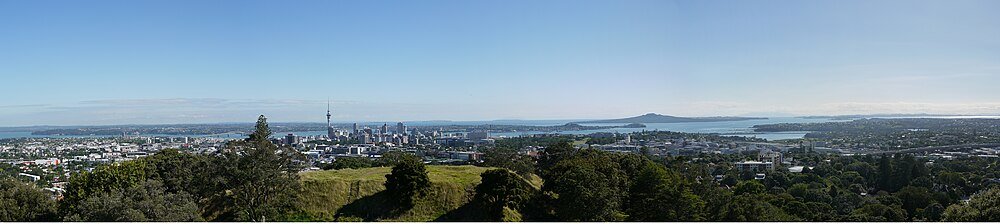 Skyline van Auckland met Sky Tower en groen Panoramisch uitzicht op de skyline van Auckland met de Sky Tower, weelderig groen en omringende waterlichamen onder een heldere blauwe lucht