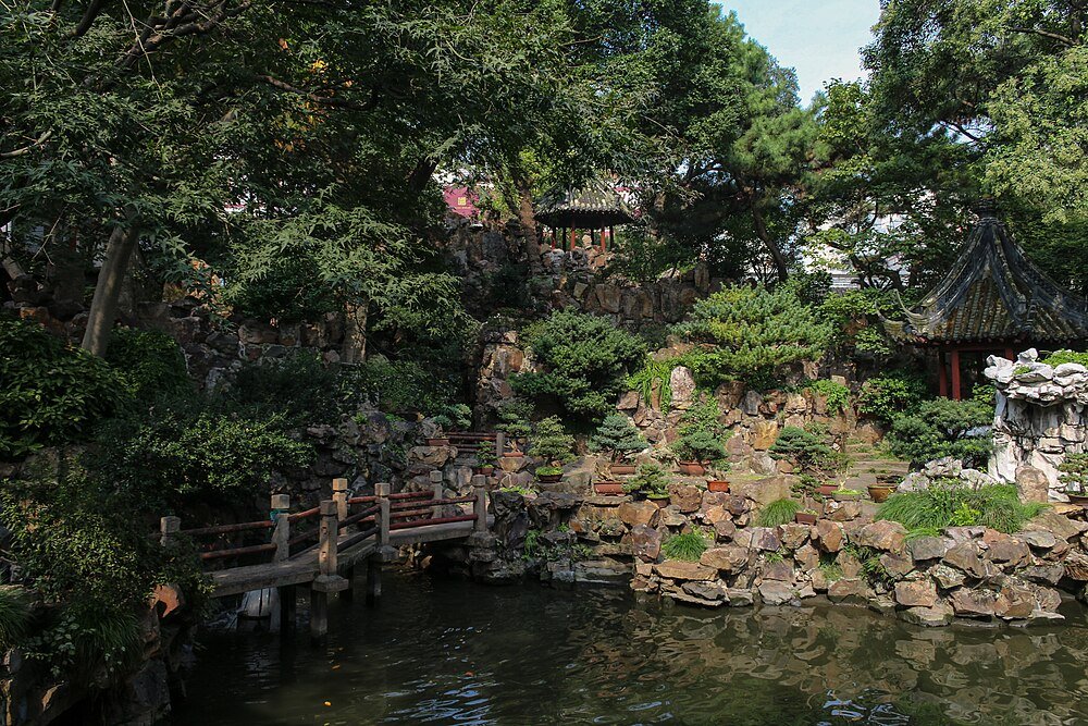 Traditionele Chinese tuin met stenen brug en vijver Traditionele Chinese tuin met stenen brug, weelderig groen, bonsaibomen en een serene vijver die de natuurlijke omgeving weerspiegelt