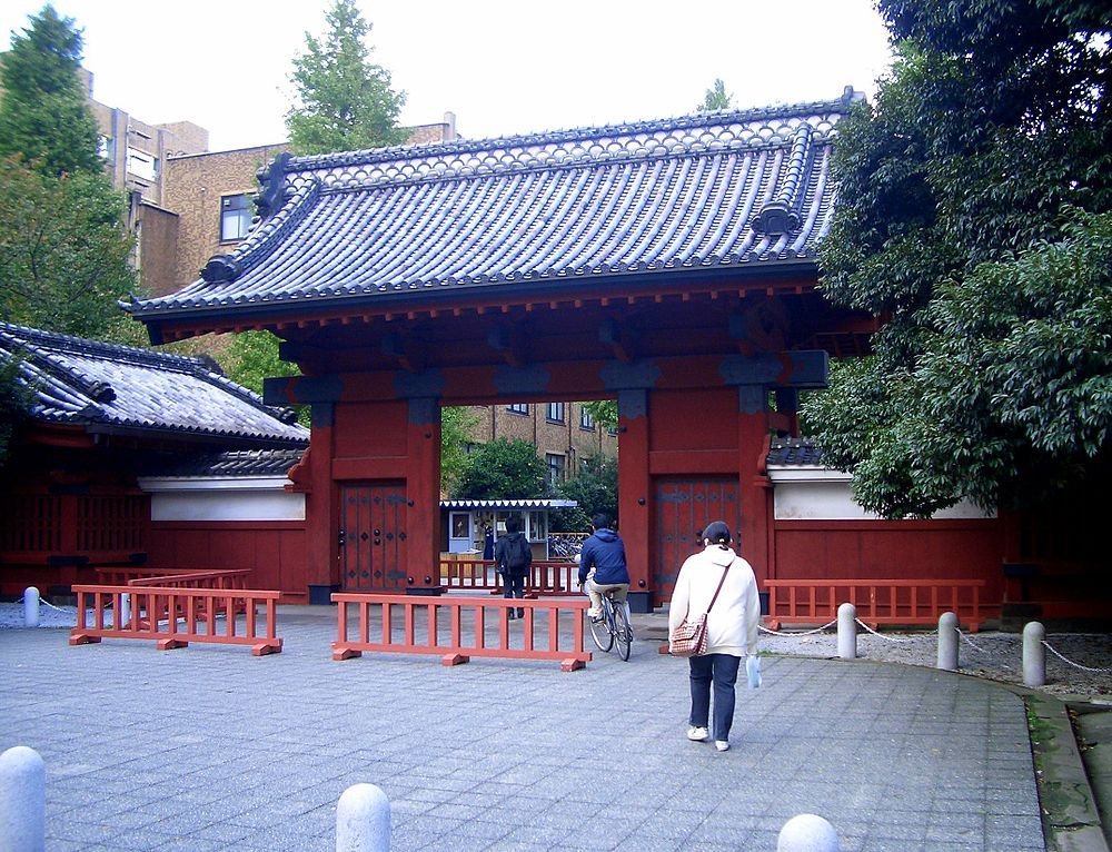 Traditionele Japanse rode poort met pannendak Traditionele Japanse rode poort met pannendak en mensen die in stedelijke omgeving lopen en fietsen