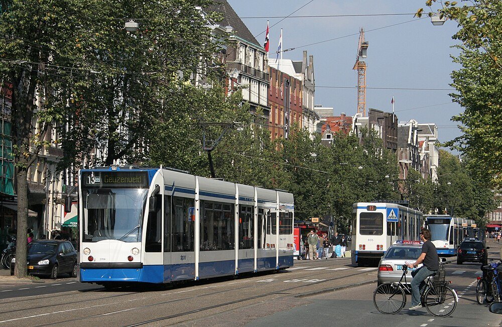Blauw-witte tram op drukke Amsterdamse straat Moderne blauw-witte tram die door een drukke stedelijke straat rijdt met fietsers en auto's in het centrum van Amsterdam
