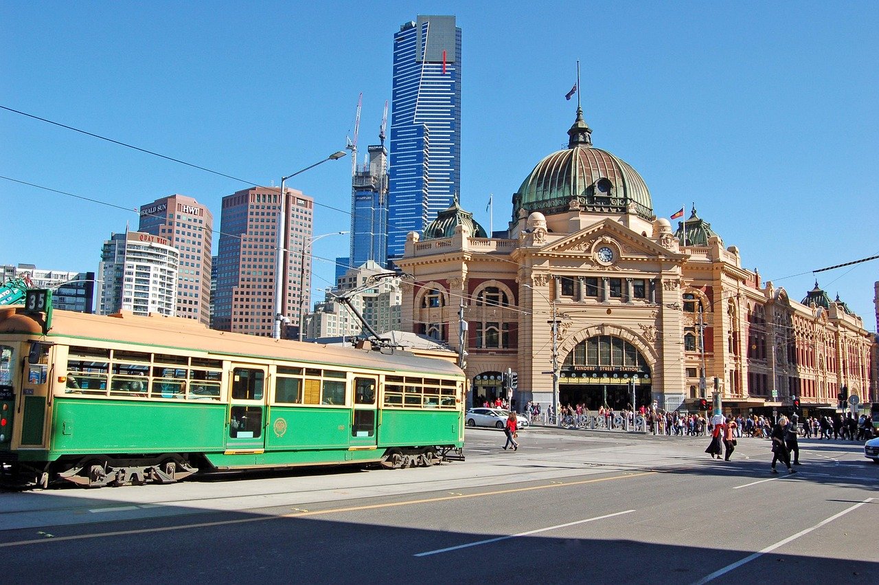 Historisch Flinders Street Station met groene tram en moderne wolkenkrabbers in Melbourne stad onder heldere blauwe lucht