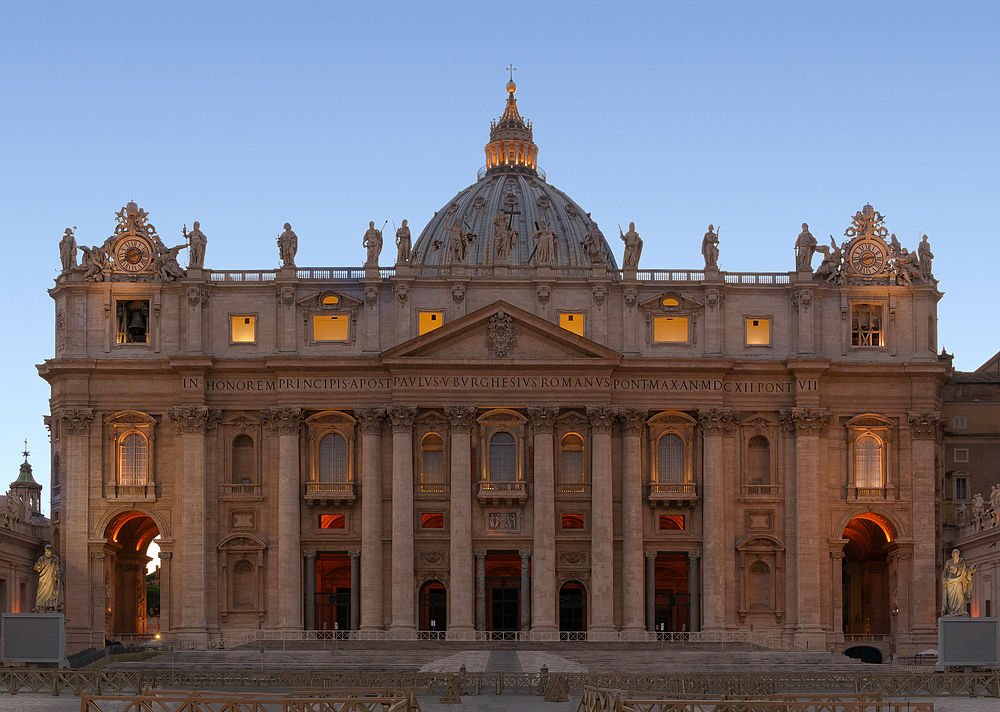 Vooraanzicht van de Sint-Pietersbasiliek in Vaticaanstad tijdens zonsondergang met verlichte ramen en beelden op het dak