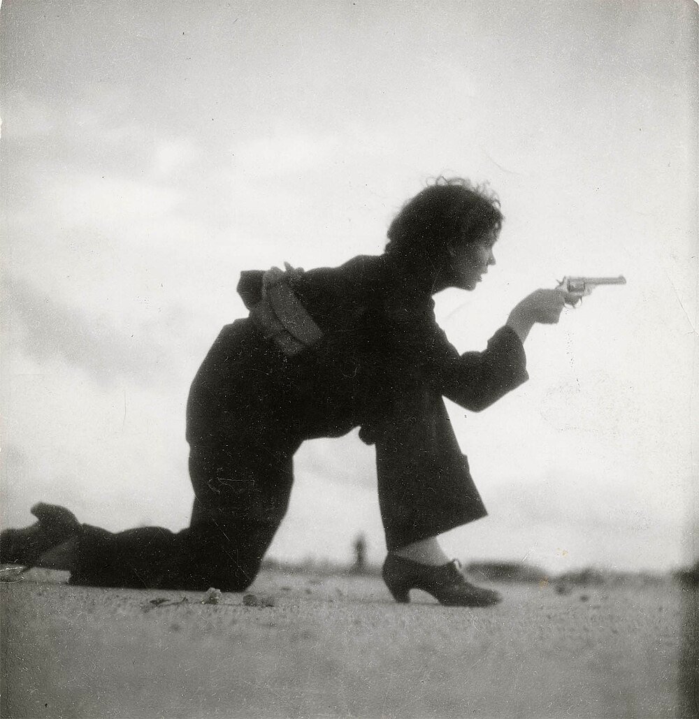 Vrouw knielend en een revolverpistool buitenshuis richtend Zwart-witfoto van een vrouw op hakken die knielt en een revolverpistool buitenshuis richt, vintage stijl