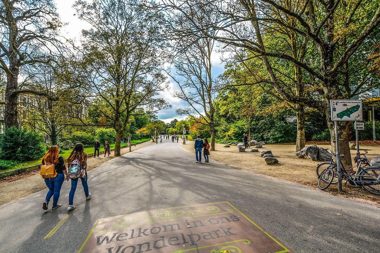 Mensen wandelen en fietsen in het Vondelpark Amsterdam met bomen en bewegwijzering die bezoekers welkom heten in het park