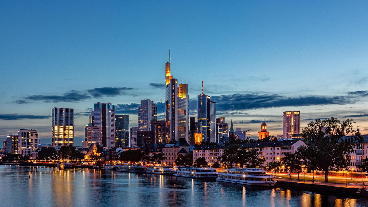 Skyline van de stad Frankfurt bij schemering met rivier en boten Skyline van de stad Frankfurt bij schemering met verlichte wolkenkrabbers en rivierboten die op het water weerspiegelen